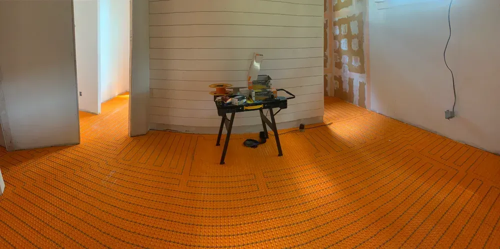 Orange radiant floor heating installation in a room, with tools on a table and white walls.