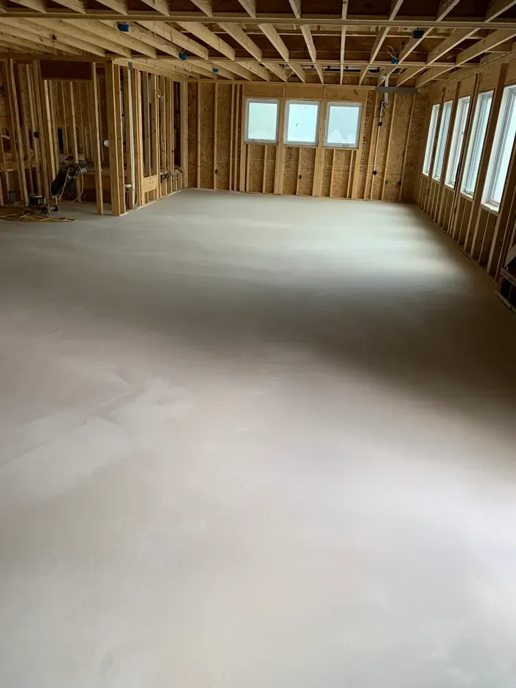 Interior view of a room under construction with wood framing and a smooth, light-colored concrete floor.