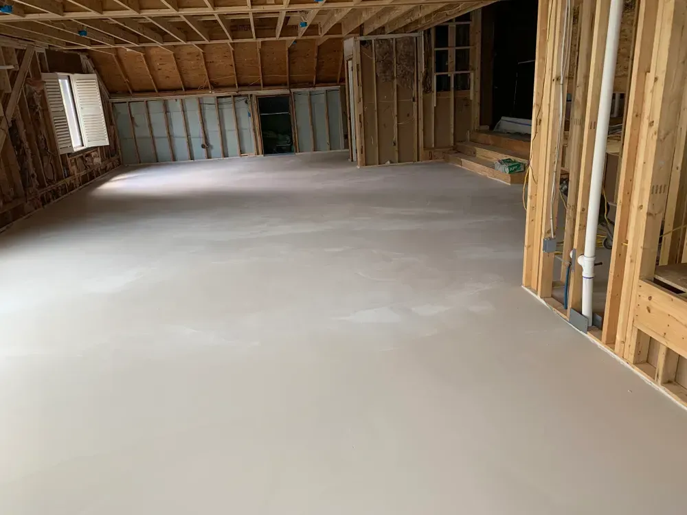 Interior of a room under construction with bare wood framing and a smooth, light-colored concrete floor.