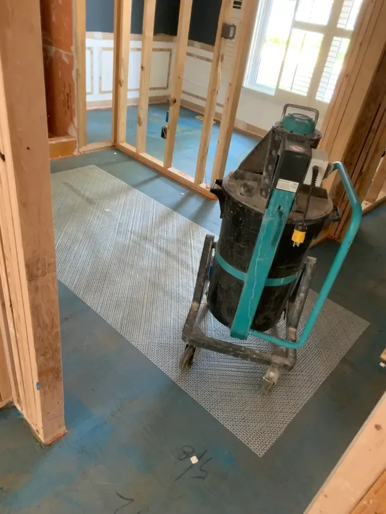 Construction site with a mixer on a wheeled cart, inside a room with wood framing and blue flooring.