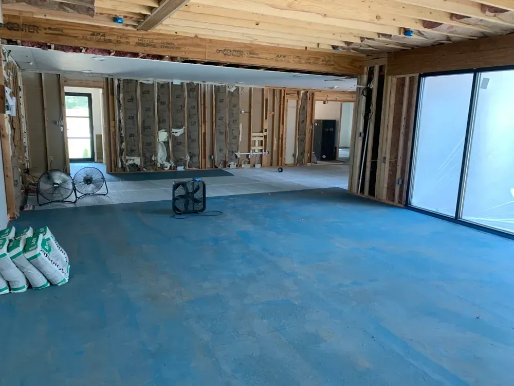Interior of a room under construction, with blue flooring and exposed wooden framing.