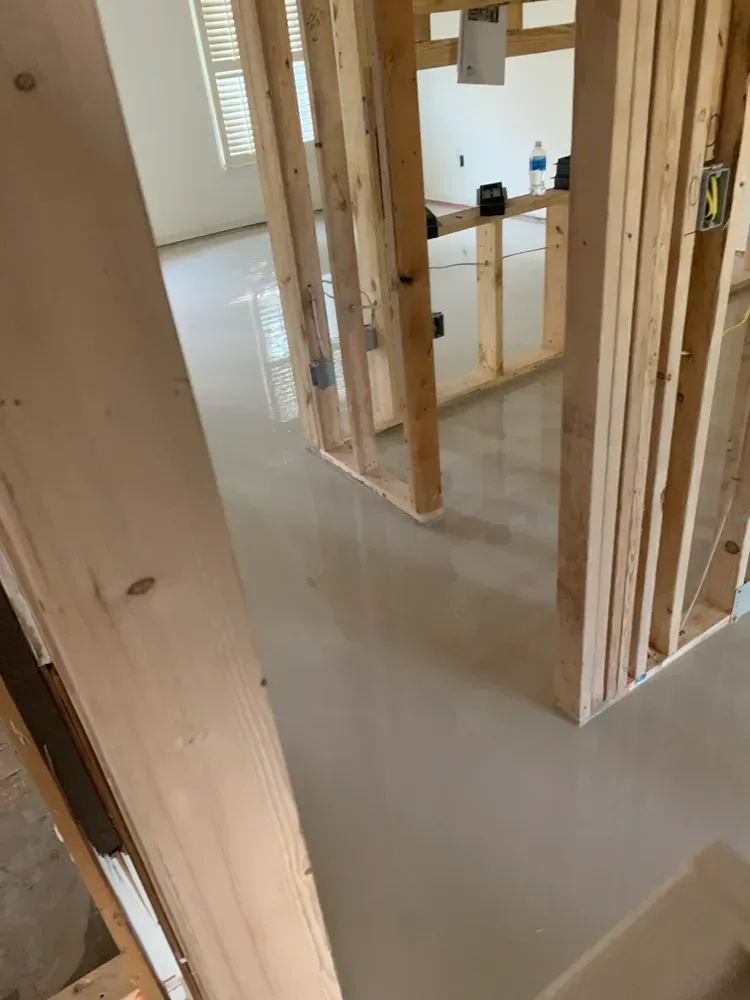 Interior view of a building under construction. Framing with a smooth, light gray concrete floor.