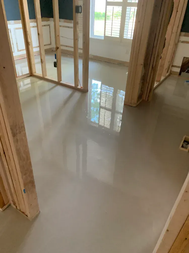Bare concrete floor in a room under construction, reflective surface, wooden framing visible.