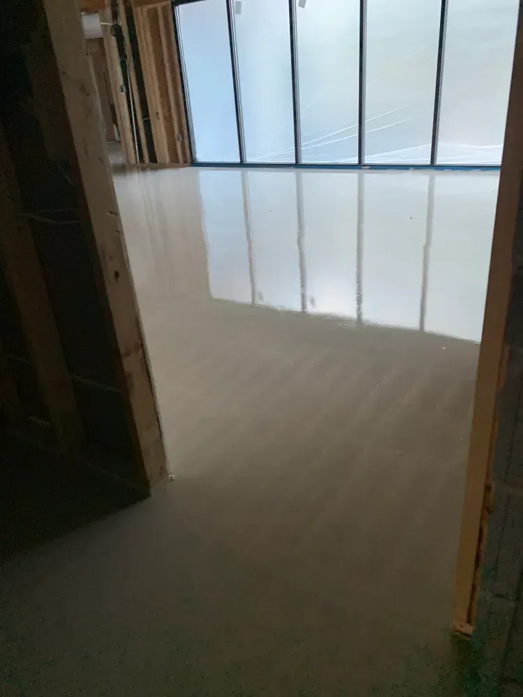 Interior of a room with a light gray smooth floor, framed by wooden studs and large windows.