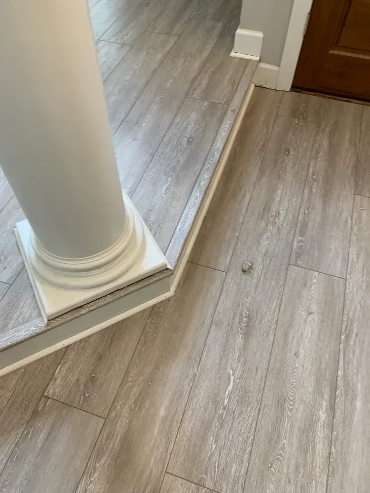 Gray wood-look flooring with a white column base. A small, round object rests on the floor.
