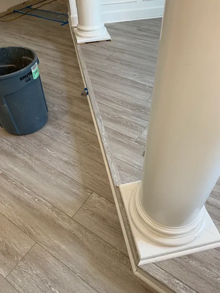 Light-colored wood-look flooring with a white trim along a column and a trash can on the left.