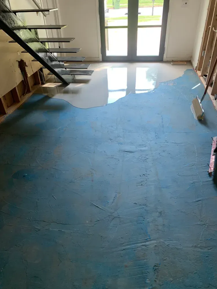 Blue floor with a portion of light-colored flooring. Staircase on the left, doorway with light coming through in the background.