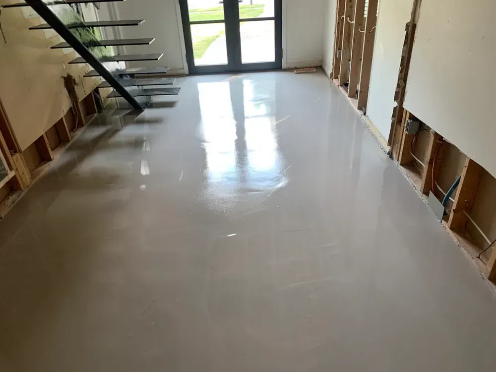Interior with freshly poured, light-colored concrete floor, exposed wall studs, and stairs.