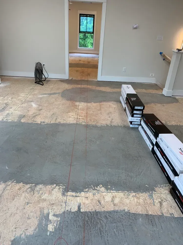 Room under construction with exposed subfloor, doorway, stacks of flooring, and a fan.