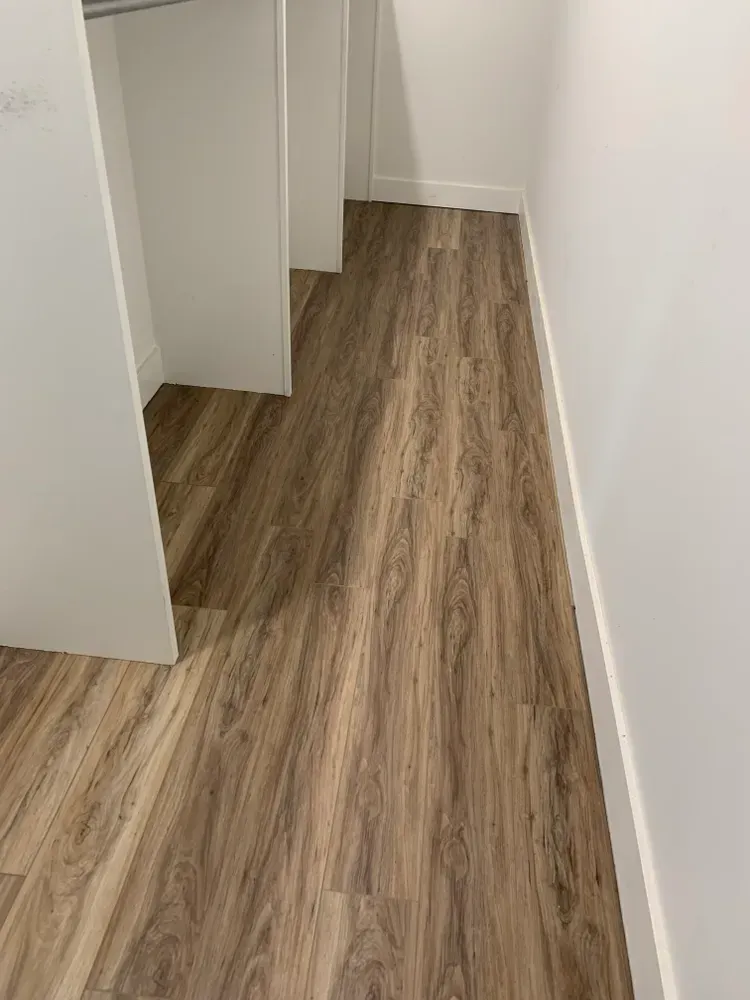 Wood-look flooring in a narrow hallway with white walls and built-in closet supports.