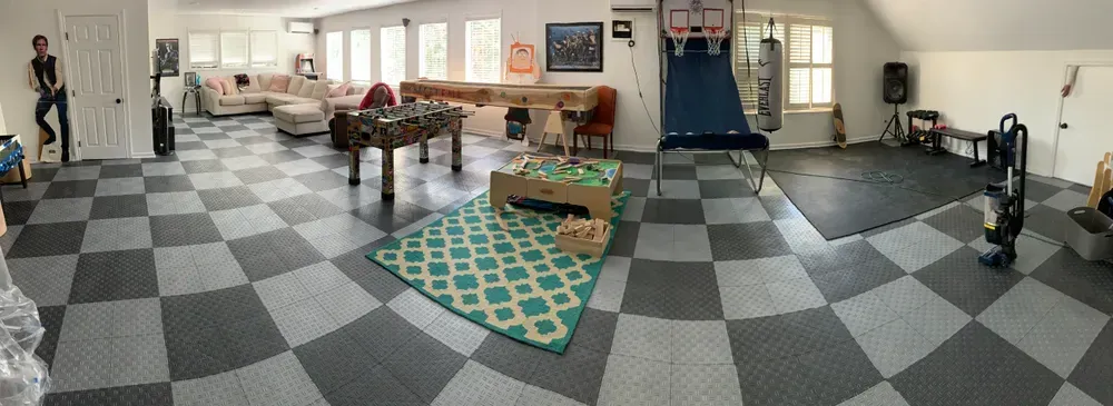 A large recreational room with foosball, basketball hoop, and checkerboard floor. A person stands near a door.