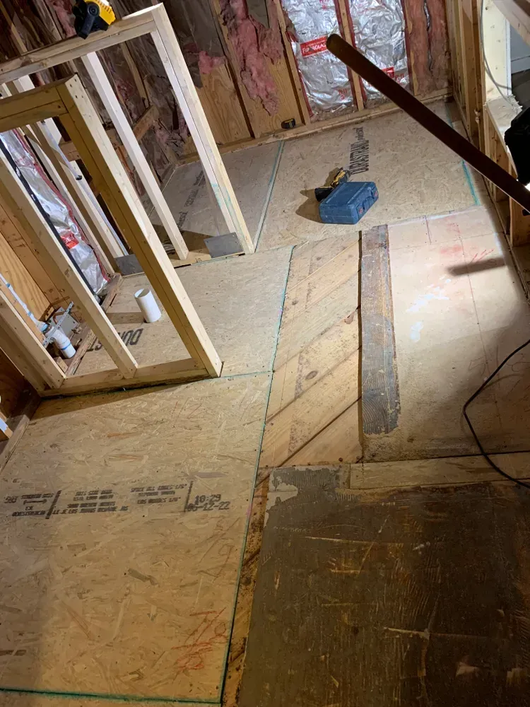 Interior of a room under construction with exposed wooden framing and flooring. Construction tools scattered.