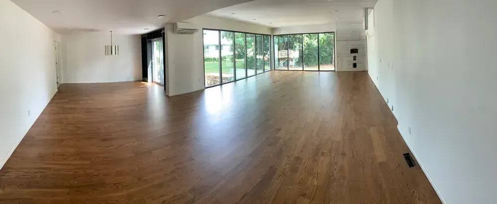 Empty, bright room with hardwood floors, large windows, and white walls.