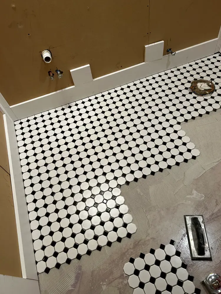 Bathroom floor being tiled with black and white penny tiles.