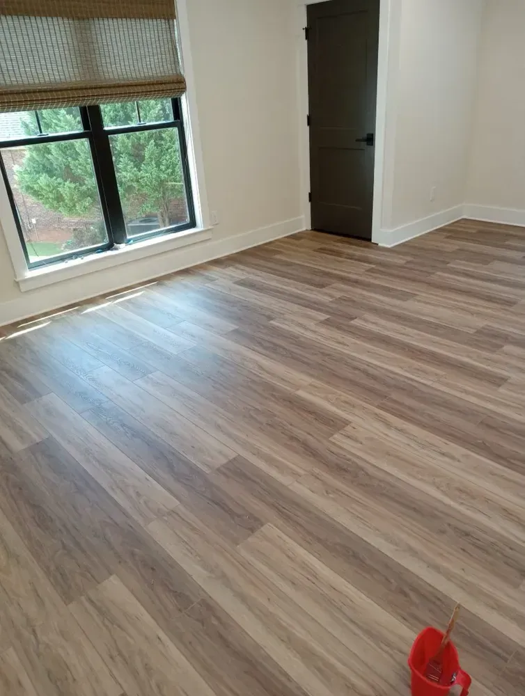 Room with wood-look flooring, window with blind, dark door, and white trim.