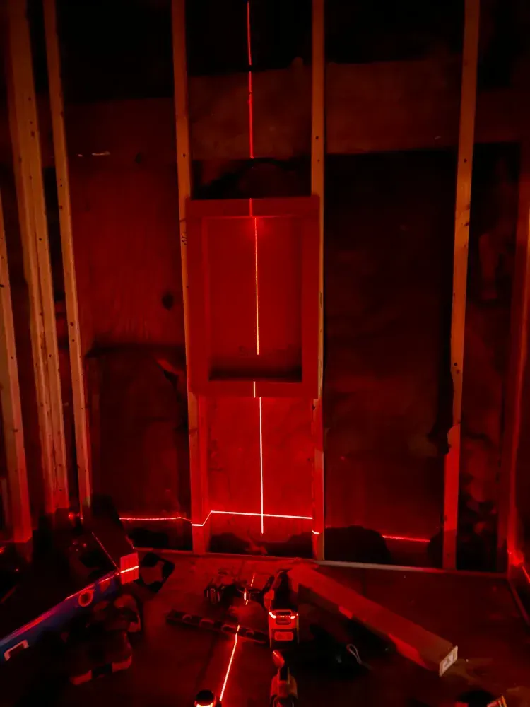 Red laser lines illuminate a construction site; framing with a central rectangular opening.