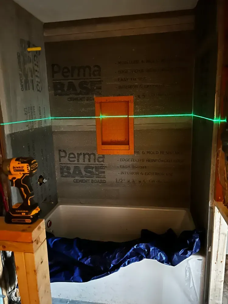 Shower remodel with green laser level. Orange niche, drill, and PermaBase cement board visible.