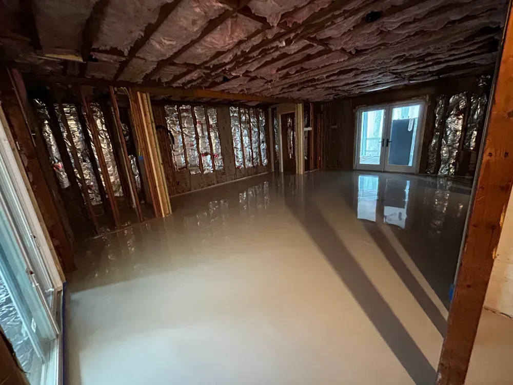 Room with unfinished walls, new light gray floor, and glass doors.