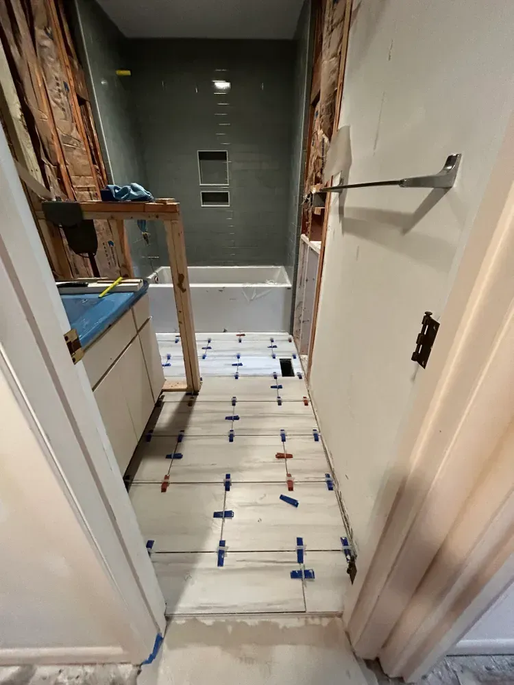 Bathroom renovation with tile floor installation in progress; vanity, bathtub, and shower visible.