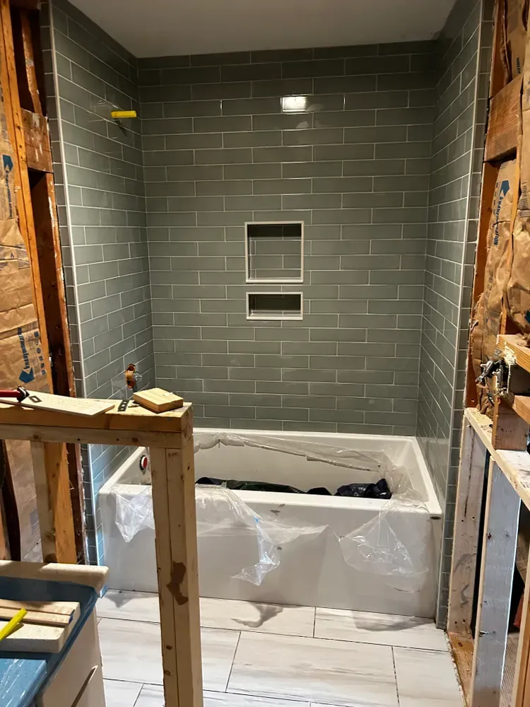 Bathroom renovation with gray tiled shower, tub, and partially exposed framing.