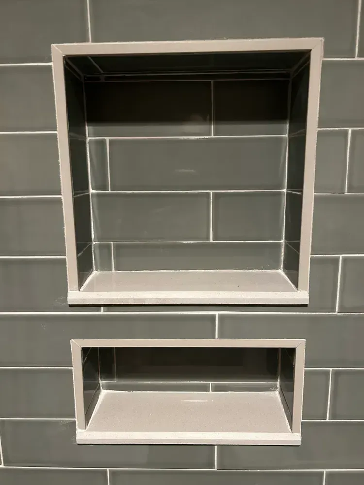 Two gray recessed shelves in a tiled shower wall.