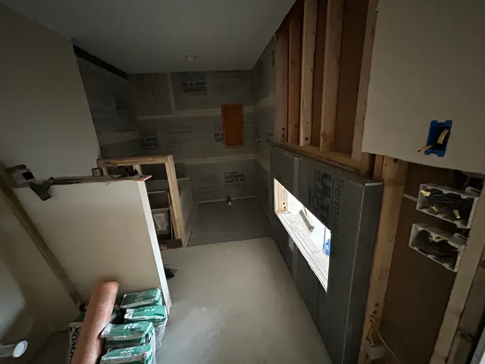 Construction site interior with exposed framing, concrete board, and electrical boxes; a partially built kitchen or bathroom.