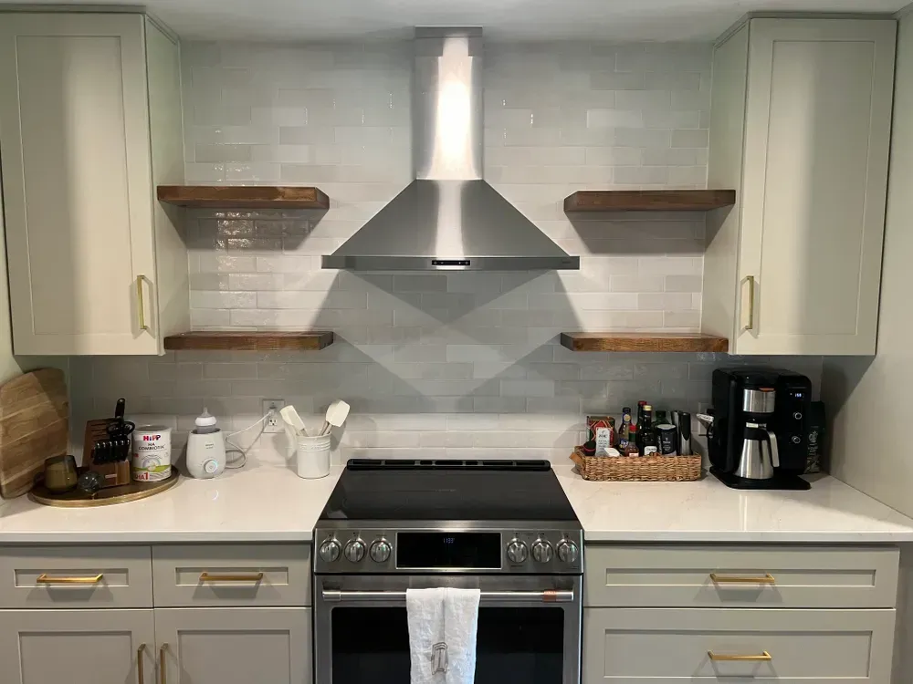 Kitchen with a stove, hood, cabinets, countertops, and floating shelves.