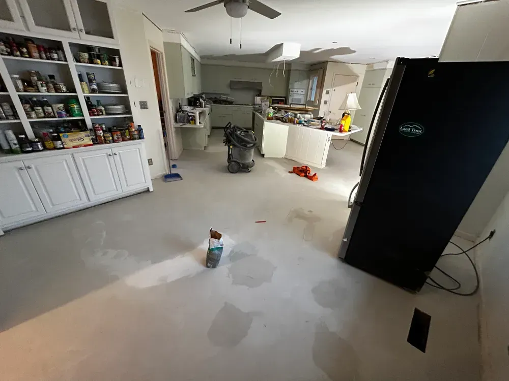 Kitchen under renovation; bare floors, cabinets, appliances, construction debris.