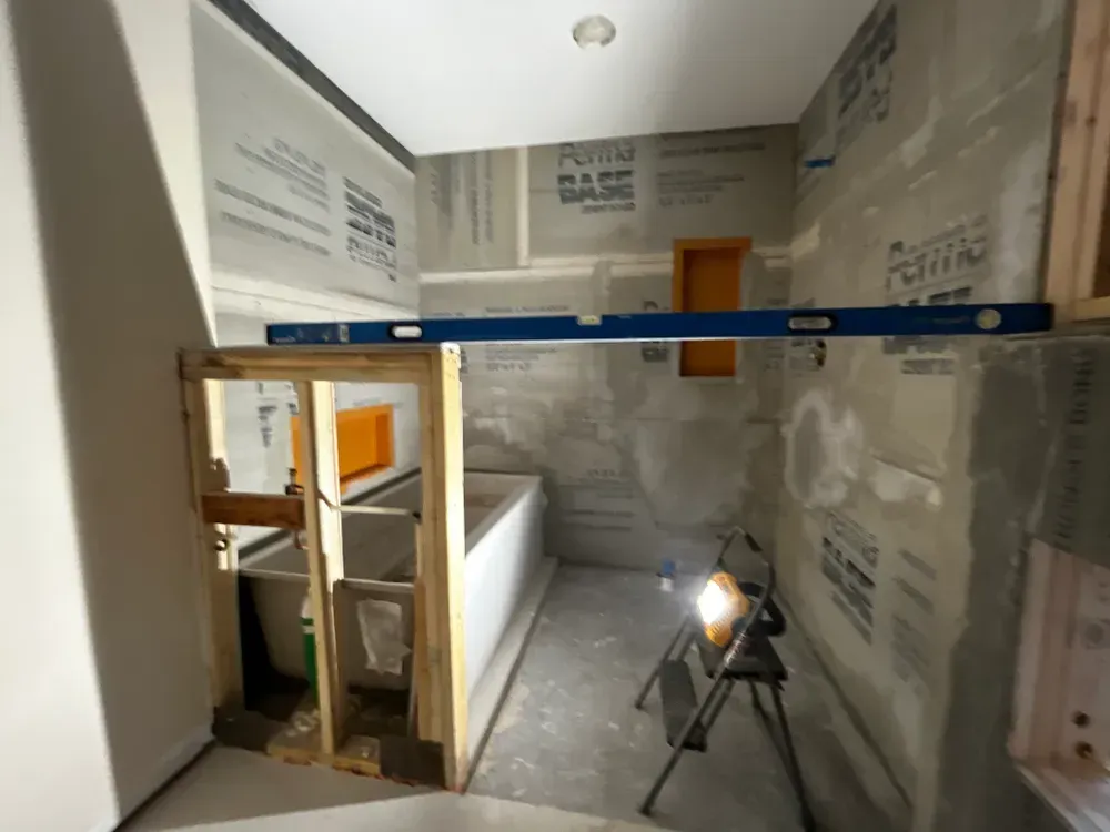 Bathroom under construction with shower area, tub, drywall, and level in place.