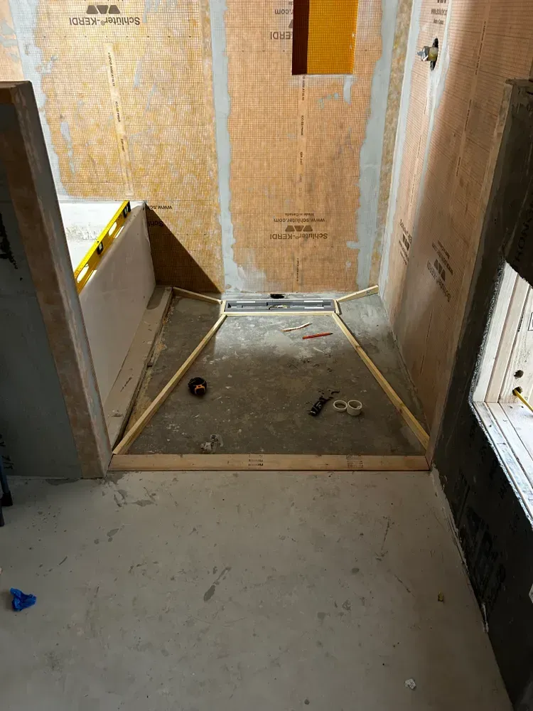 Shower under construction: wooden frame, waterproof backing, floor drain, unfinished walls.