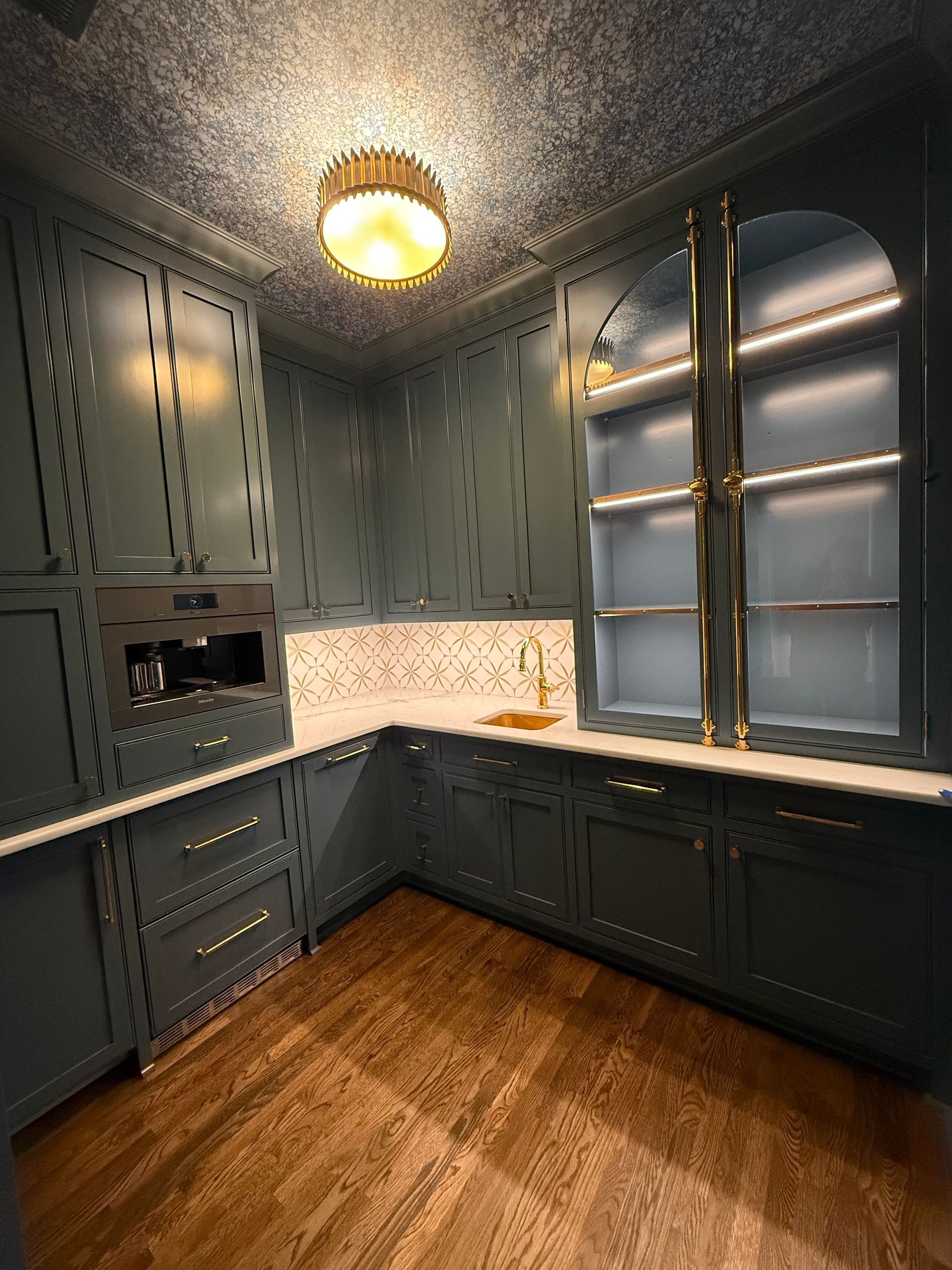 Dark teal kitchen with wood floors, marble backsplash, and gold accents.