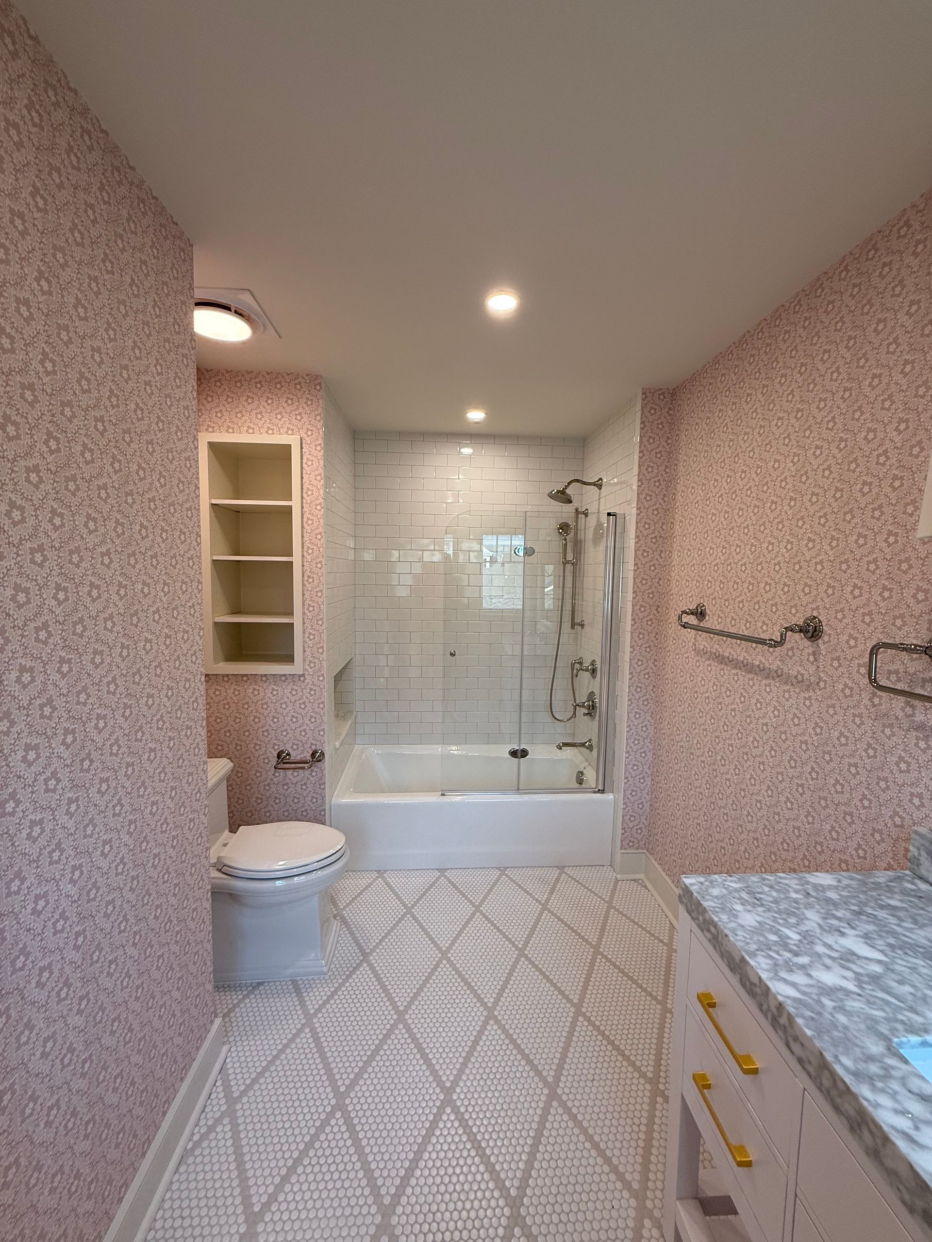 Bathroom with pink speckled walls, patterned floor, white tub/toilet, glass shower door.