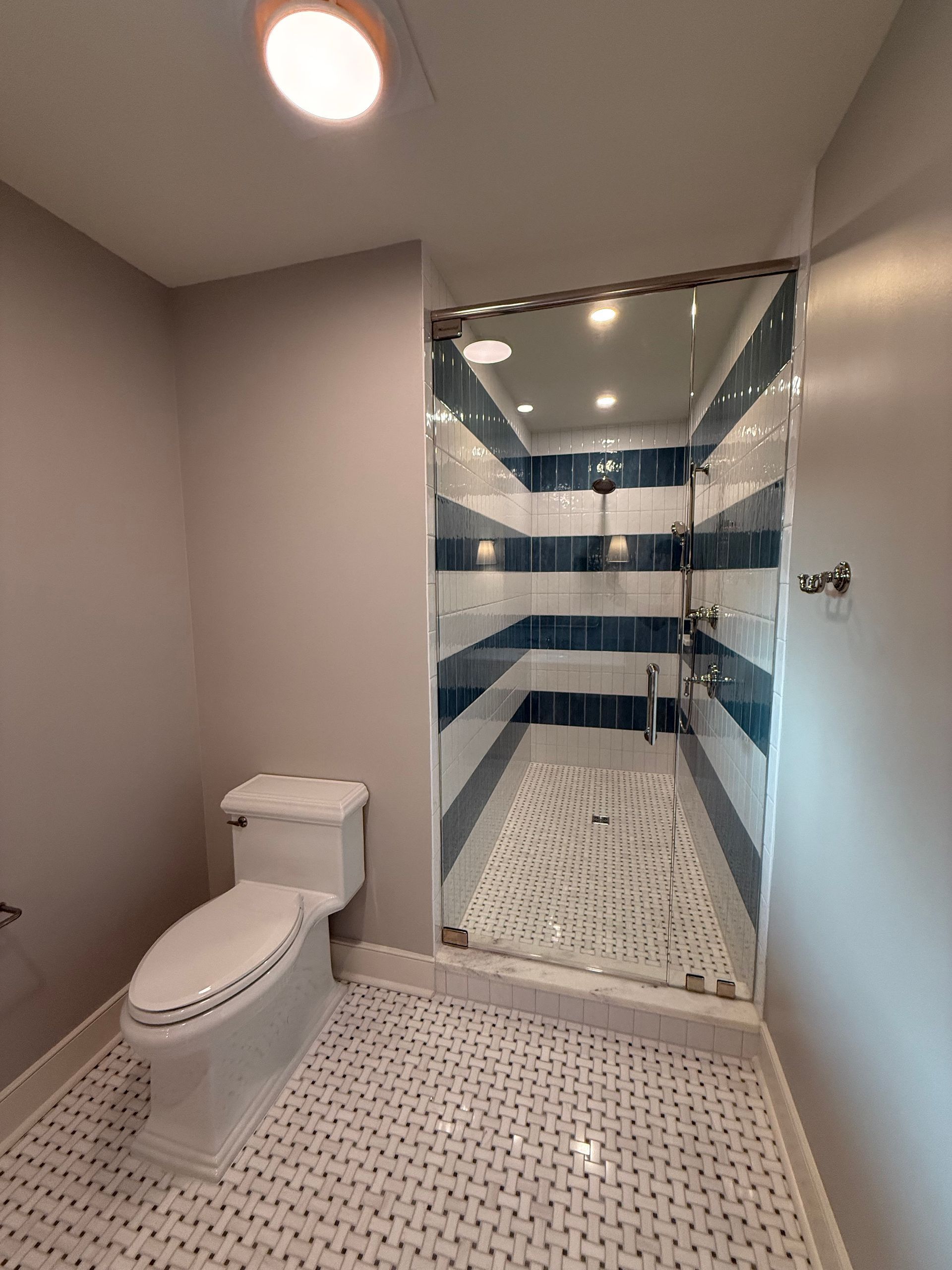 Bathroom with white toilet, blue and white striped shower, and gray walls.