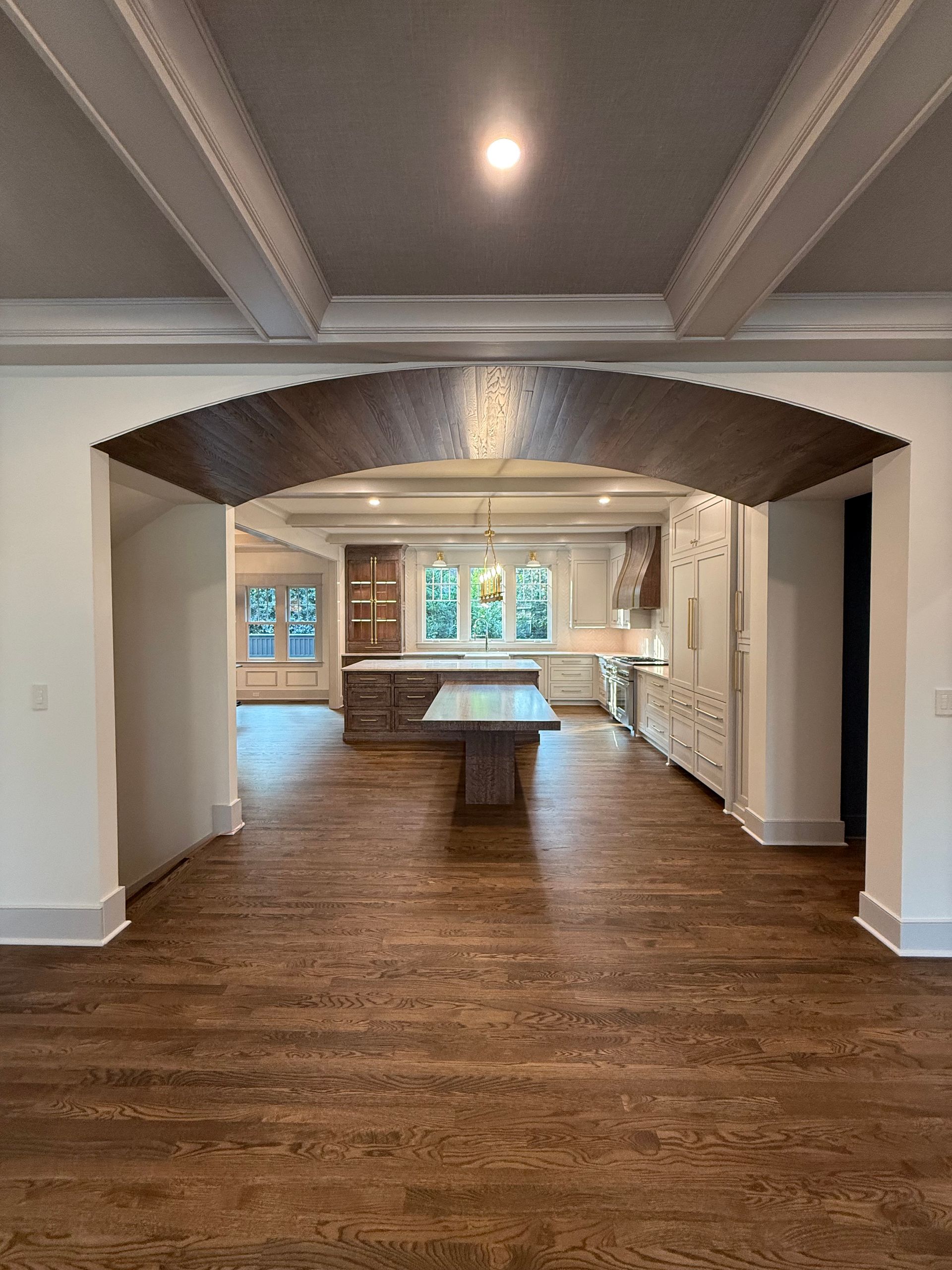 Open archway leading to a kitchen with a large island and white cabinetry; dark wood floors and ceiling beams.
