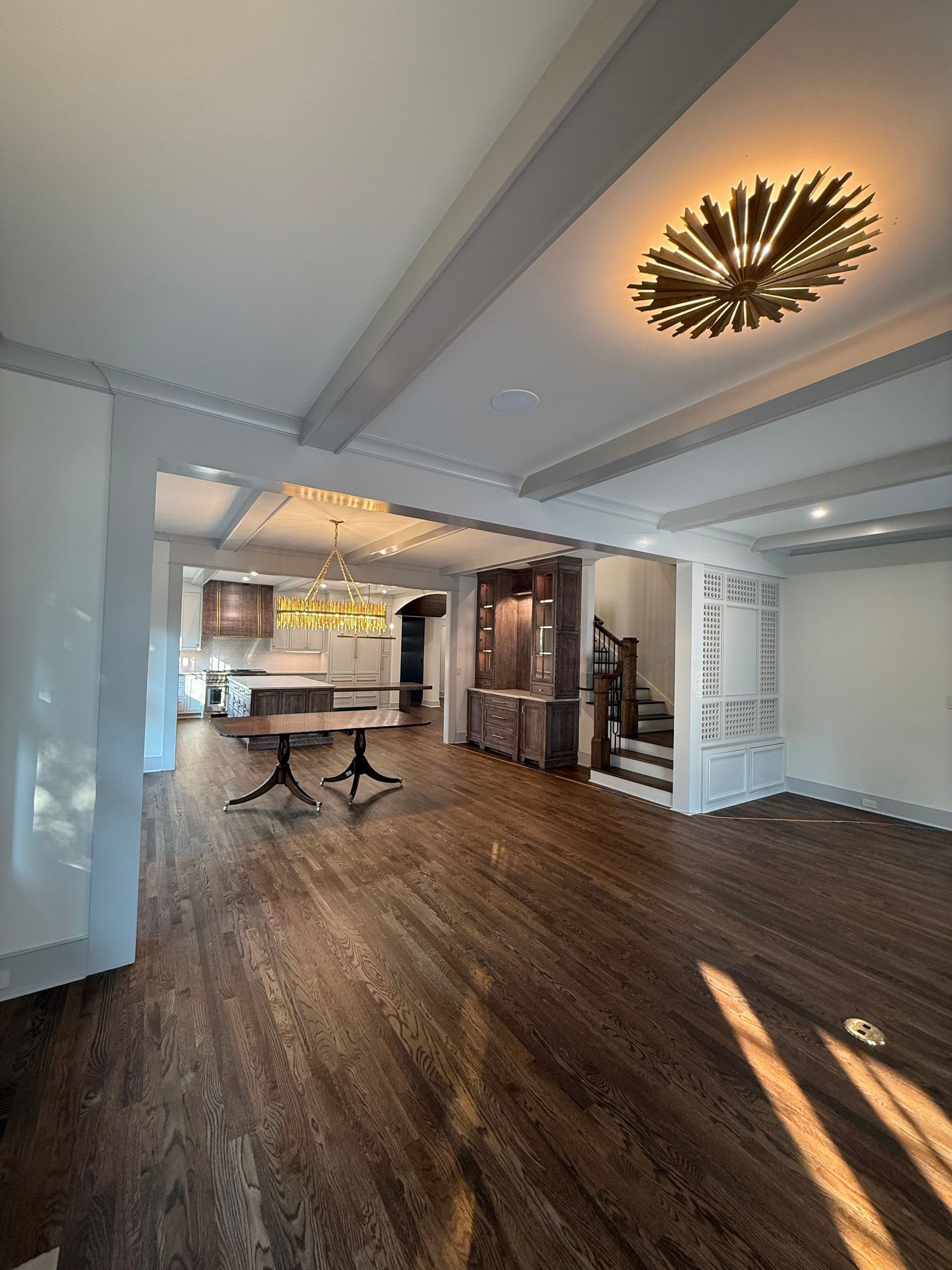 Spacious living area with dark wood floors, overhead beams, and a golden sputnik light fixture.