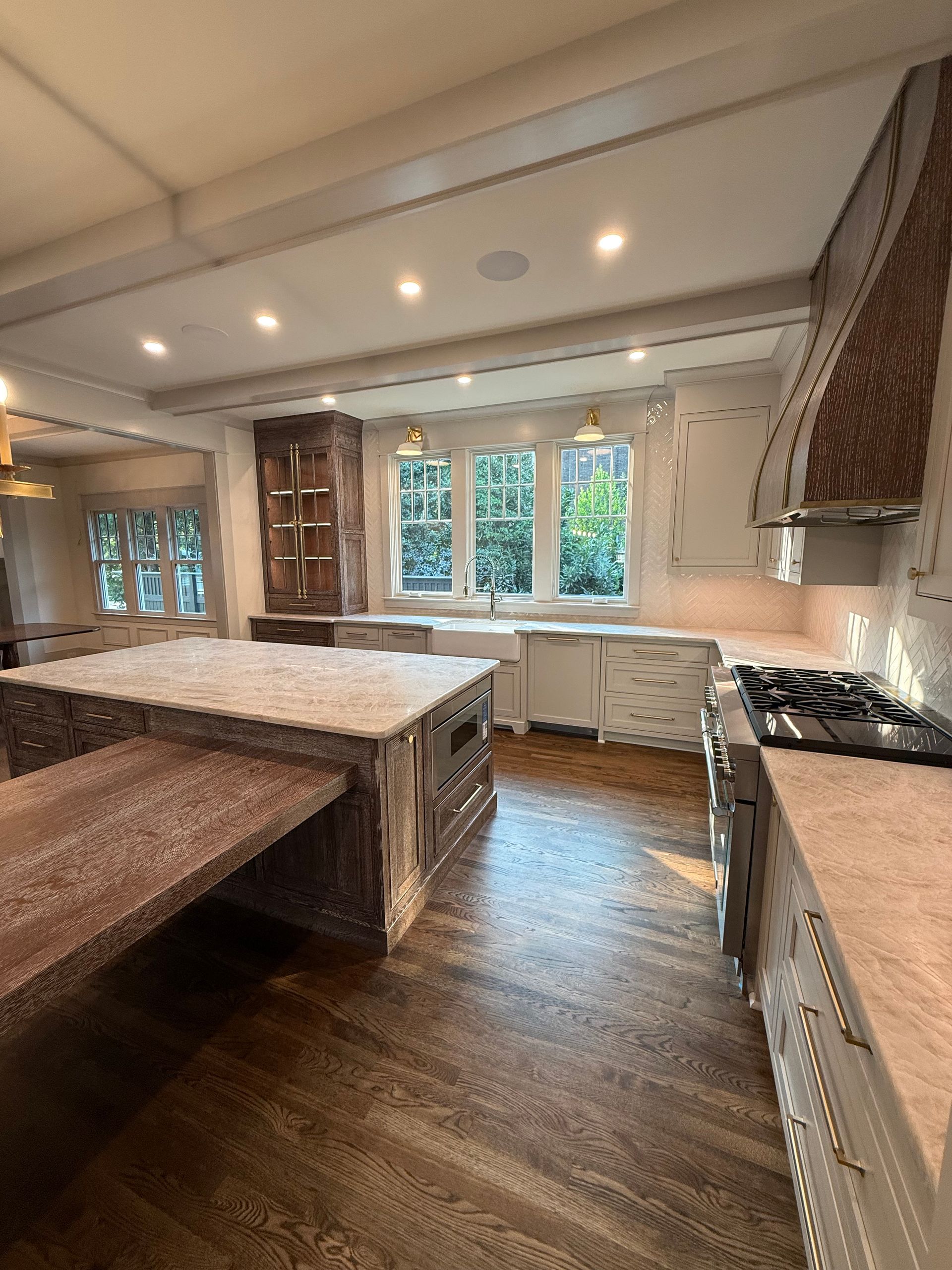 A luxury kitchen with a large island, gas range, and stone countertops. Features wood floors, custom cabinetry, and a bay window.