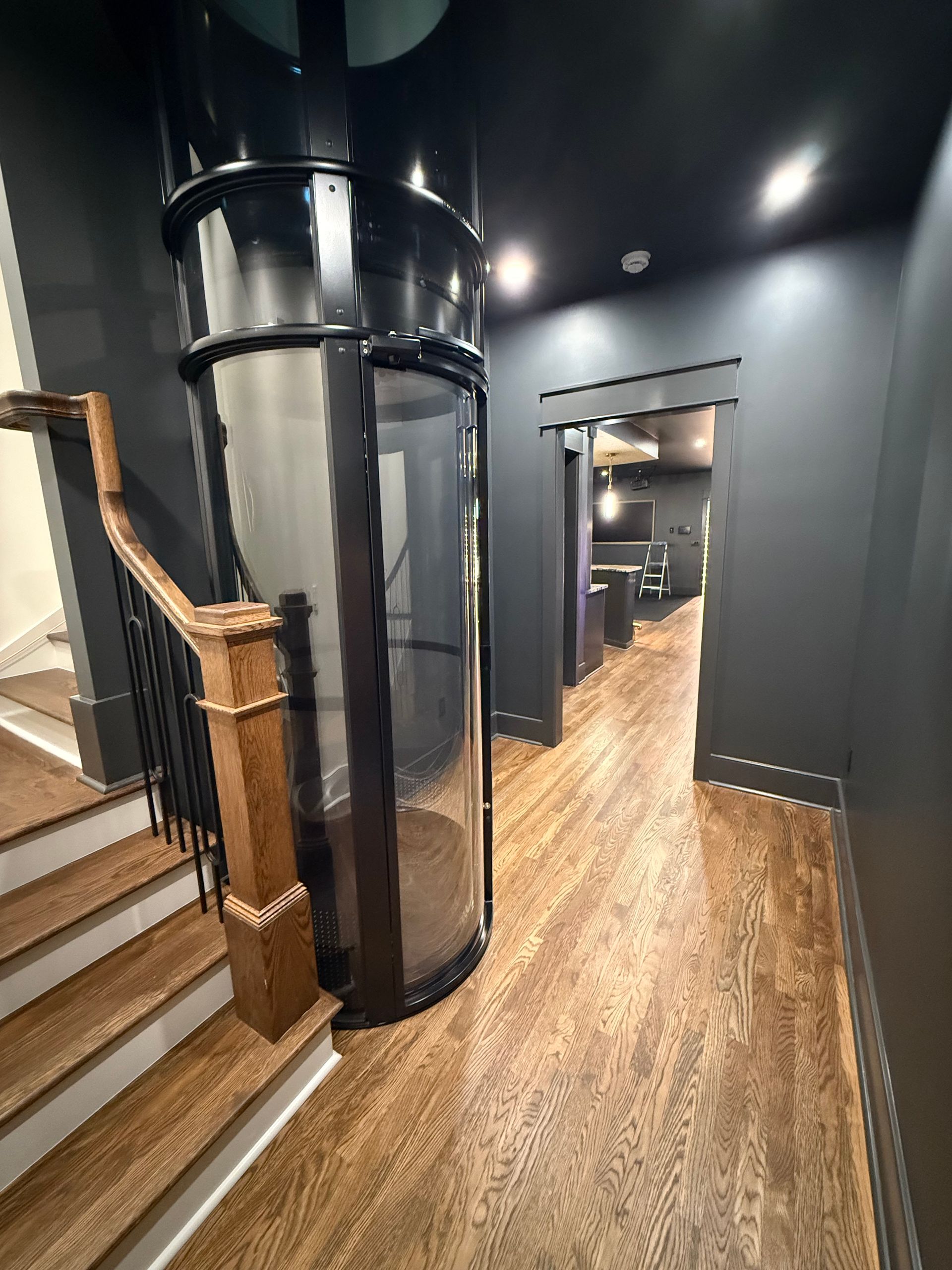 Hallway with elevator, stairs, and dark walls. Wooden floors and banister.