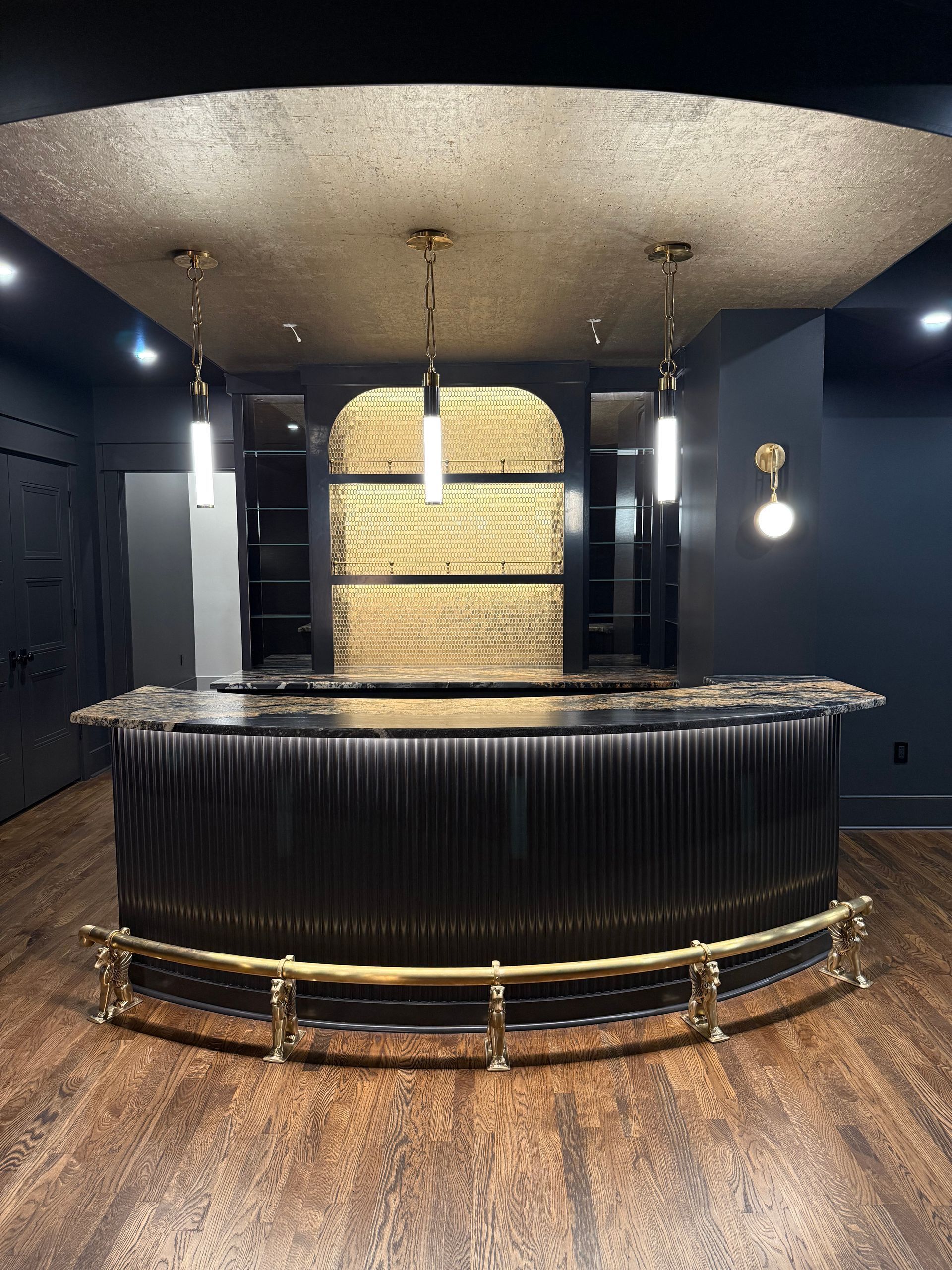 Elegant home bar with black curved facade, gold accents, and three pendant lights.