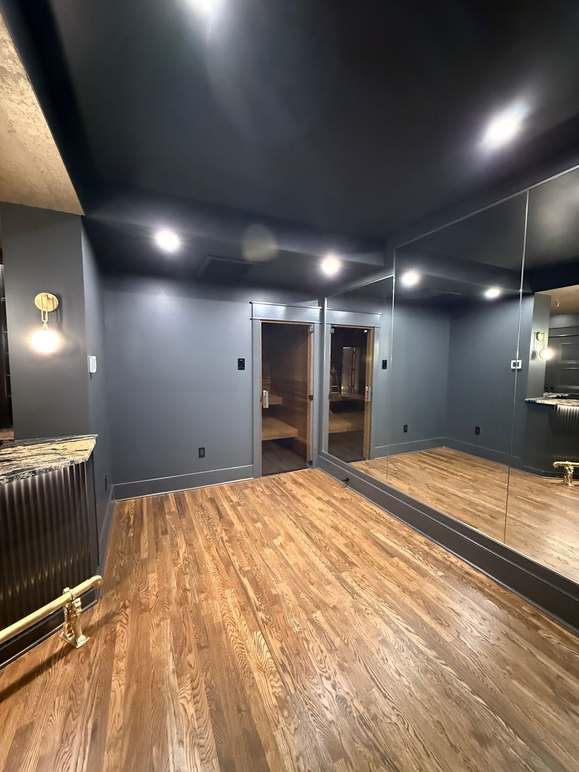 Dark-painted room with wooden floor, two doors, and a bar with gold accents.