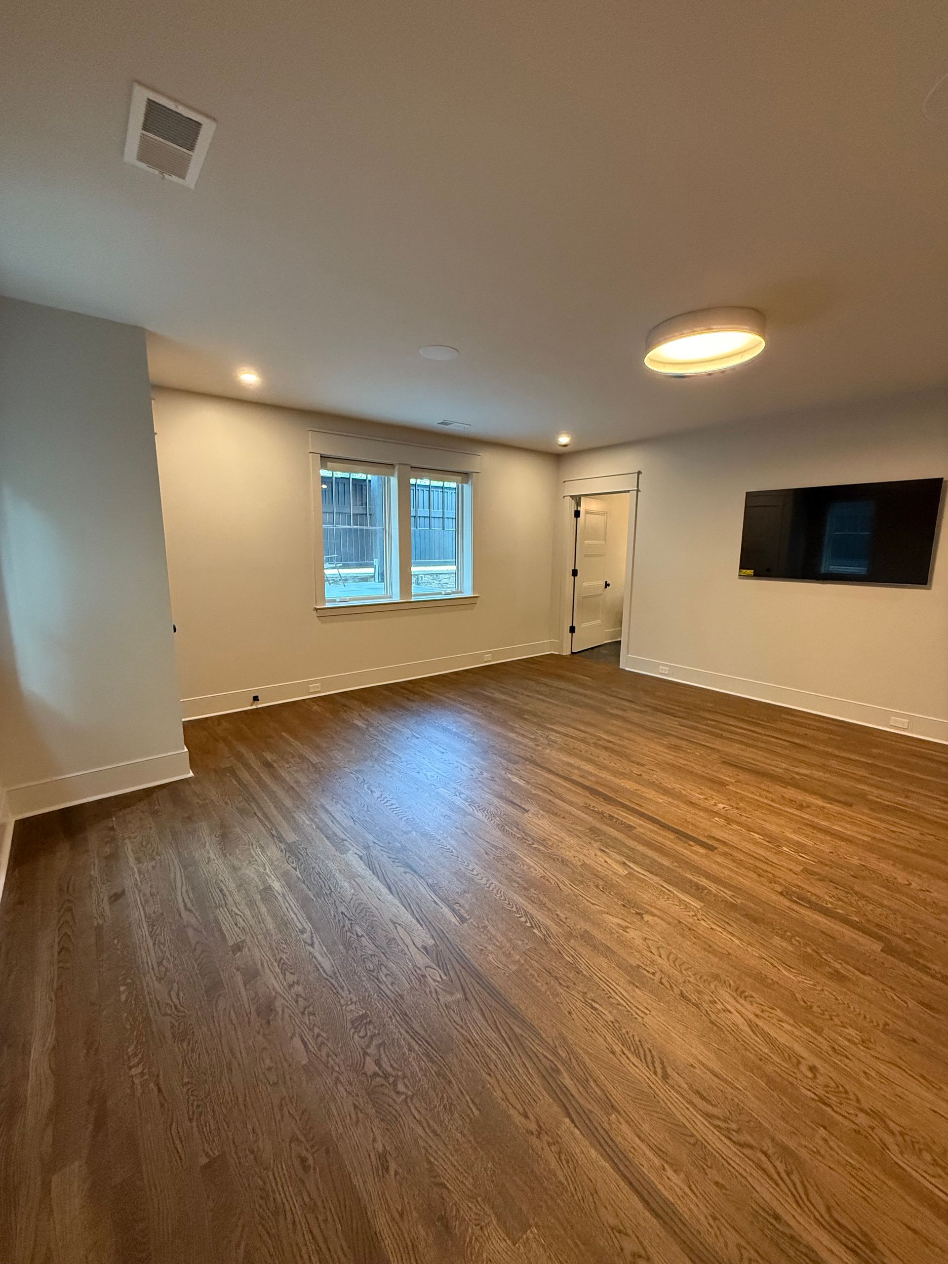 Empty living room with wood flooring, white walls, two windows, and a mounted TV.
