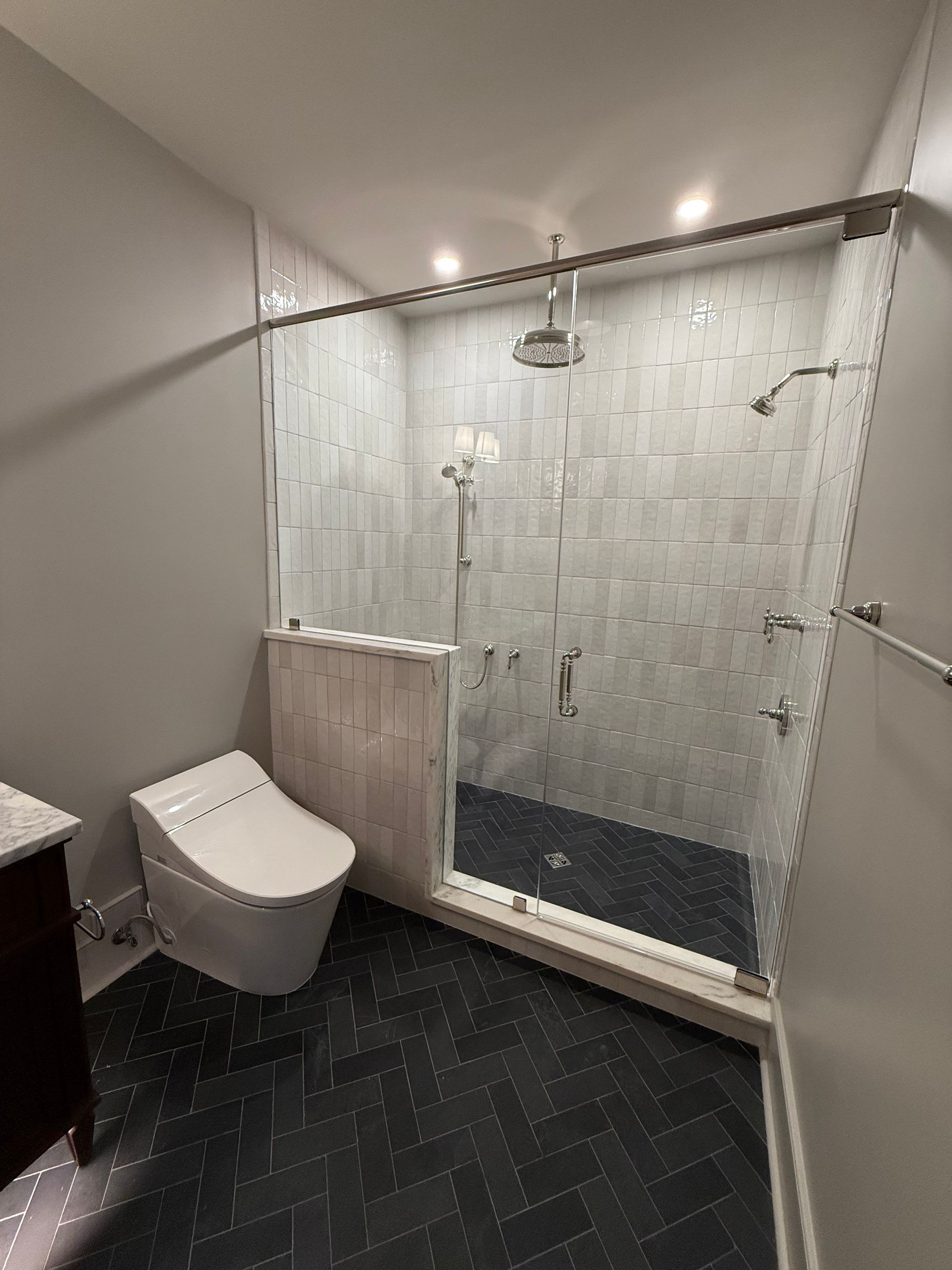 Modern bathroom with a glass shower and a high-tech toilet; gray and black tile.