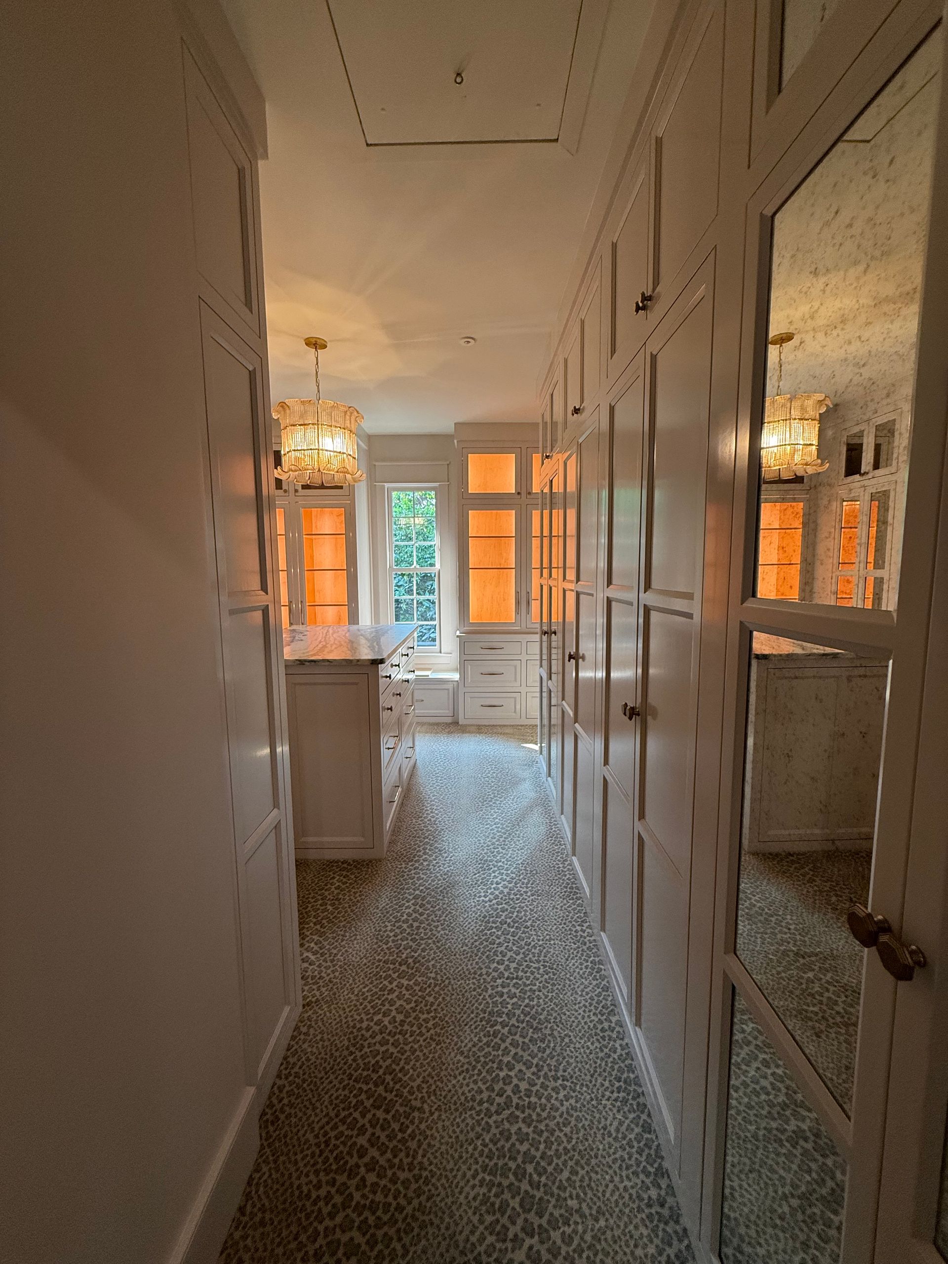 Narrow hallway with white cabinets, speckled floor, and a window at the end.