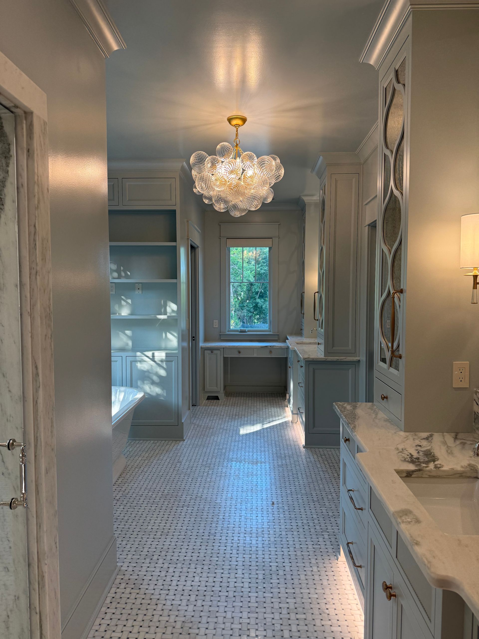 Elegant light blue bathroom with patterned tile floor, built-in storage, and a bubble chandelier.