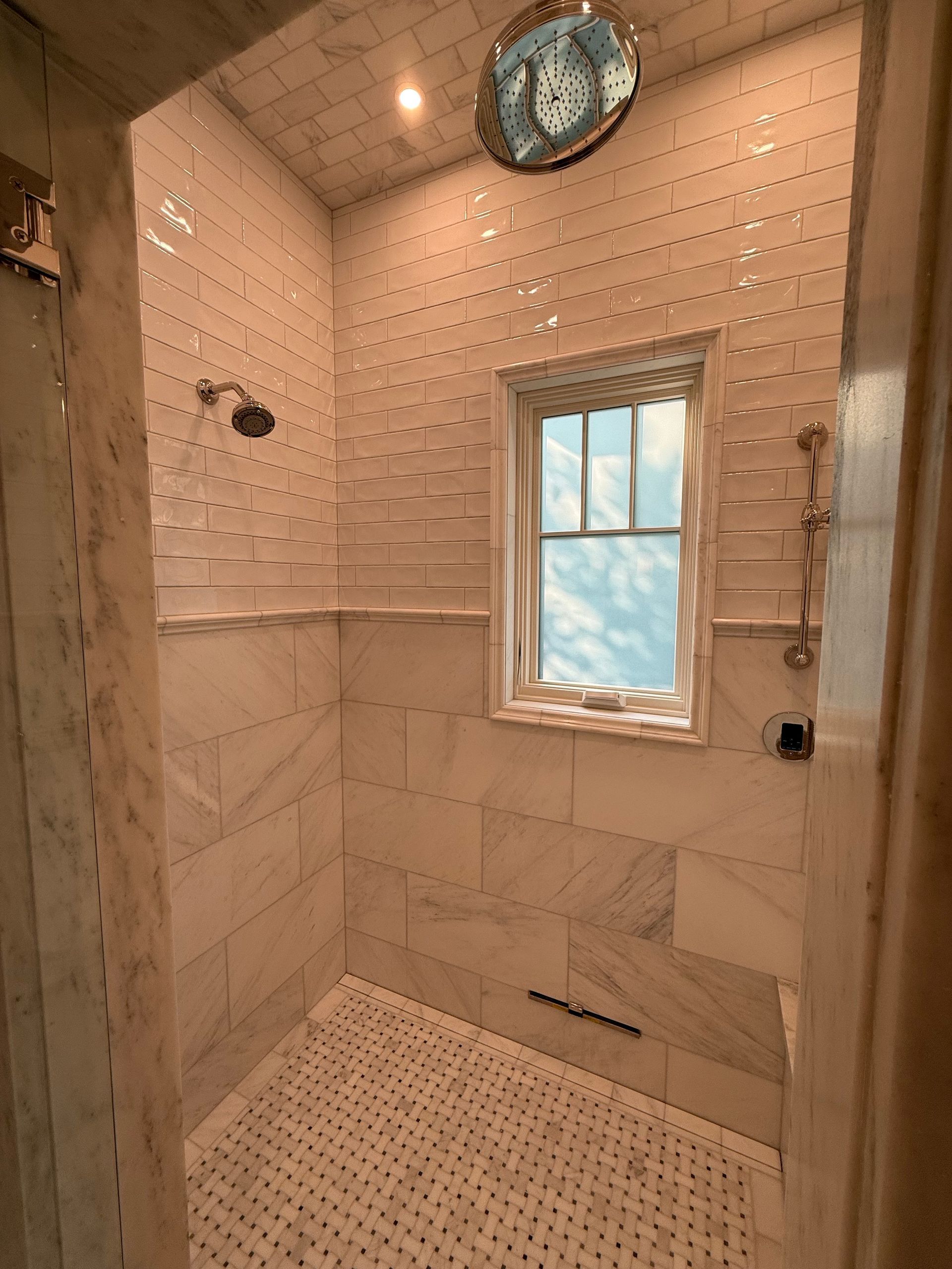 Small shower with white and tan textured tiles and a window.