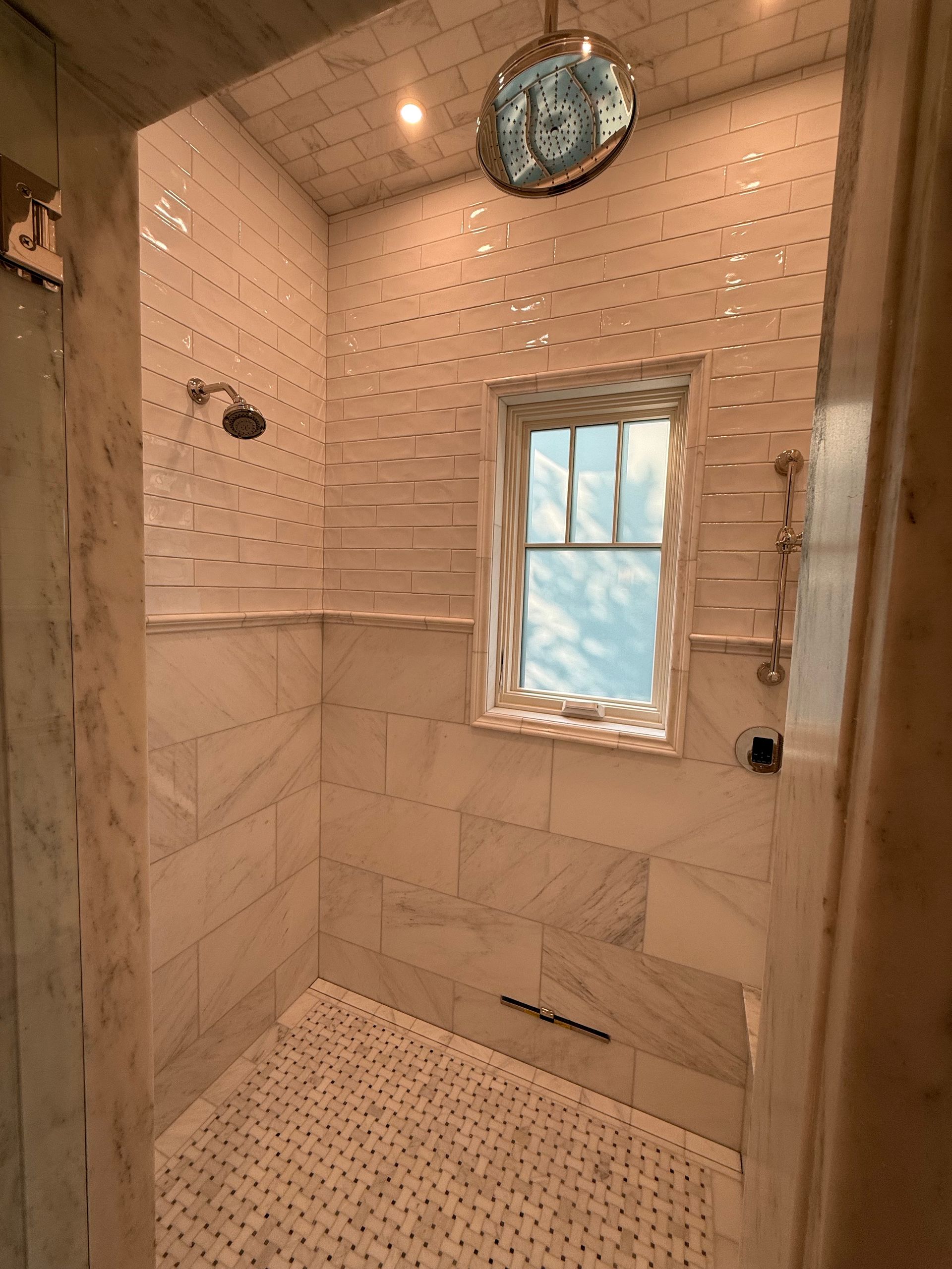 Shower with white marble tiles and a window.
