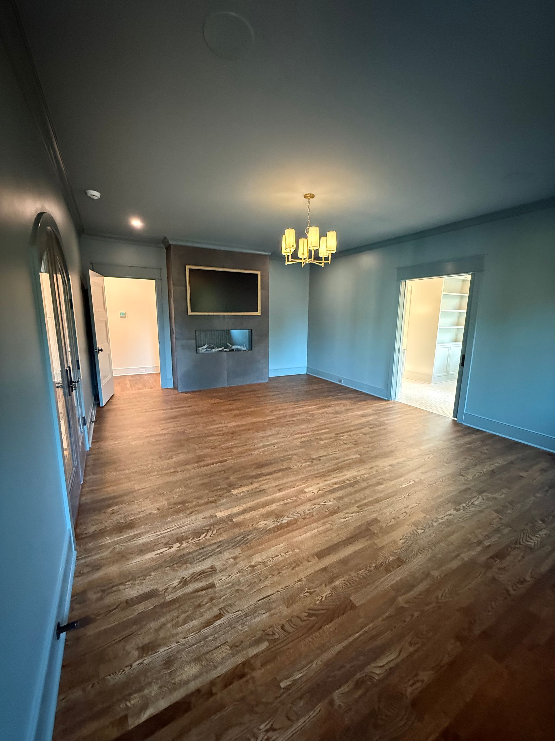 Empty room with hardwood floors, blue walls, a TV, chandelier, and doorways.