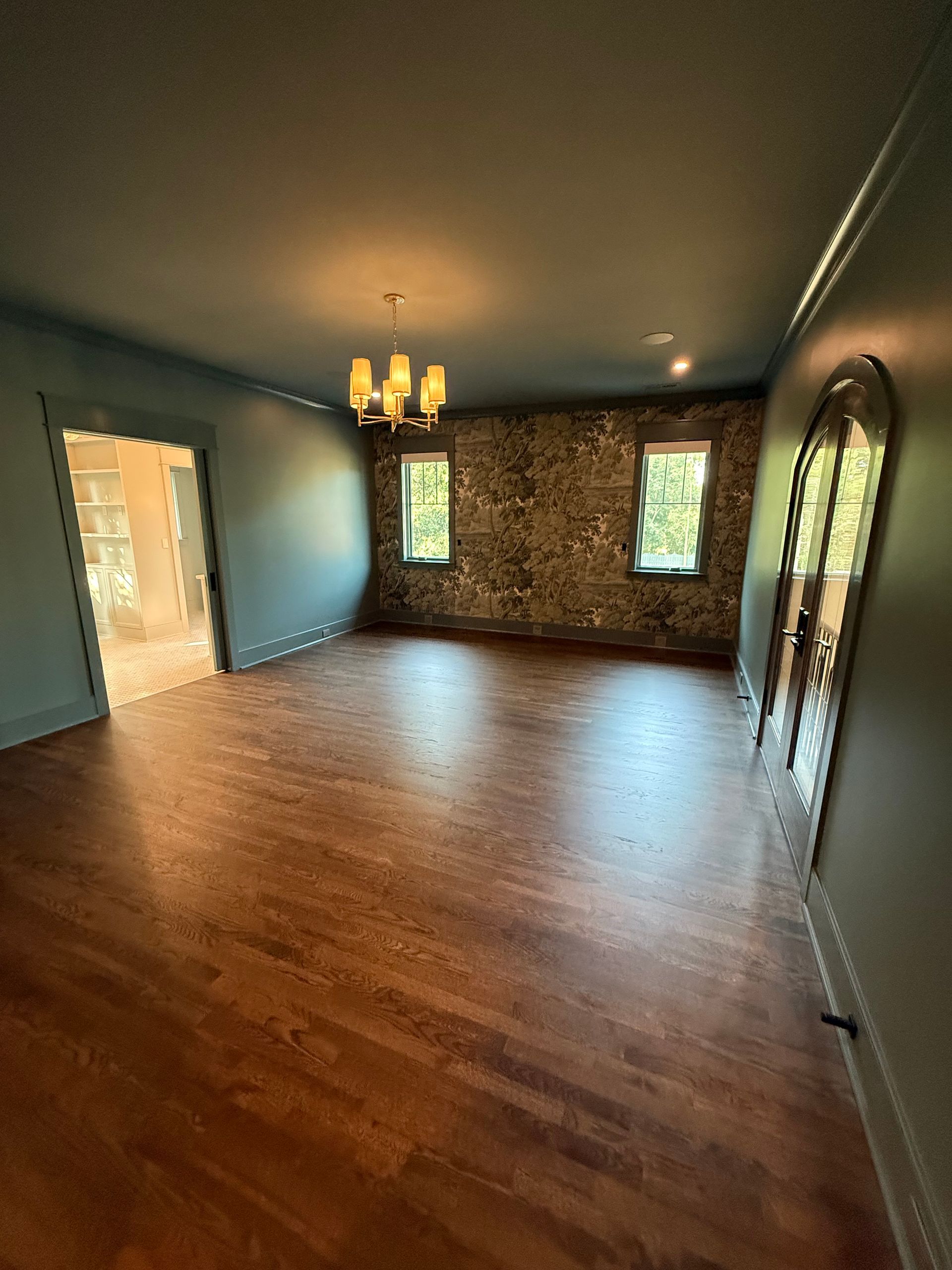 Empty room with wood floor, teal walls, exposed brick accent wall, and chandelier.