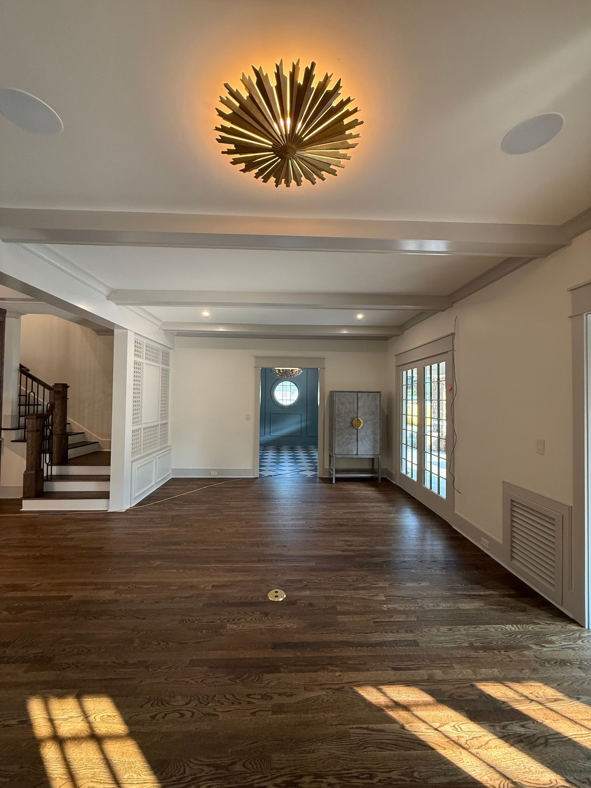 Empty living room with wood floor, recessed lighting, and ornate gold ceiling fixture.