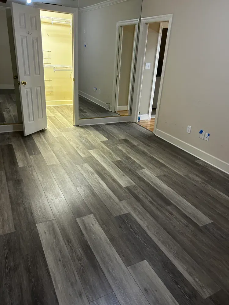 Empty room with gray wood-look flooring, white trim, two doors, and a full-length mirror.