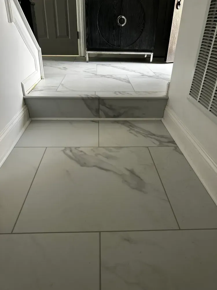 White tiled entryway with a small step leading to a dark door, and a white air vent on the right.